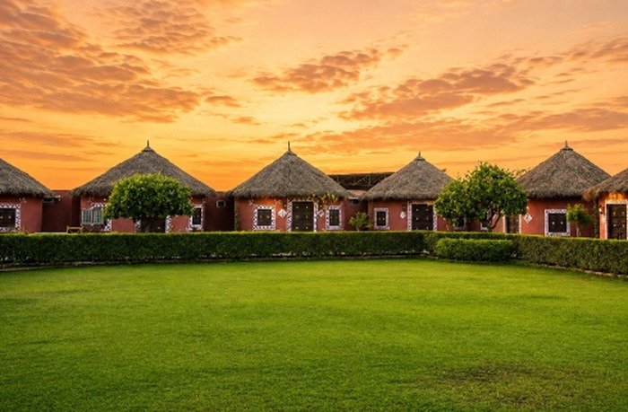 Row of thatched heritage cottages facing a green lawn